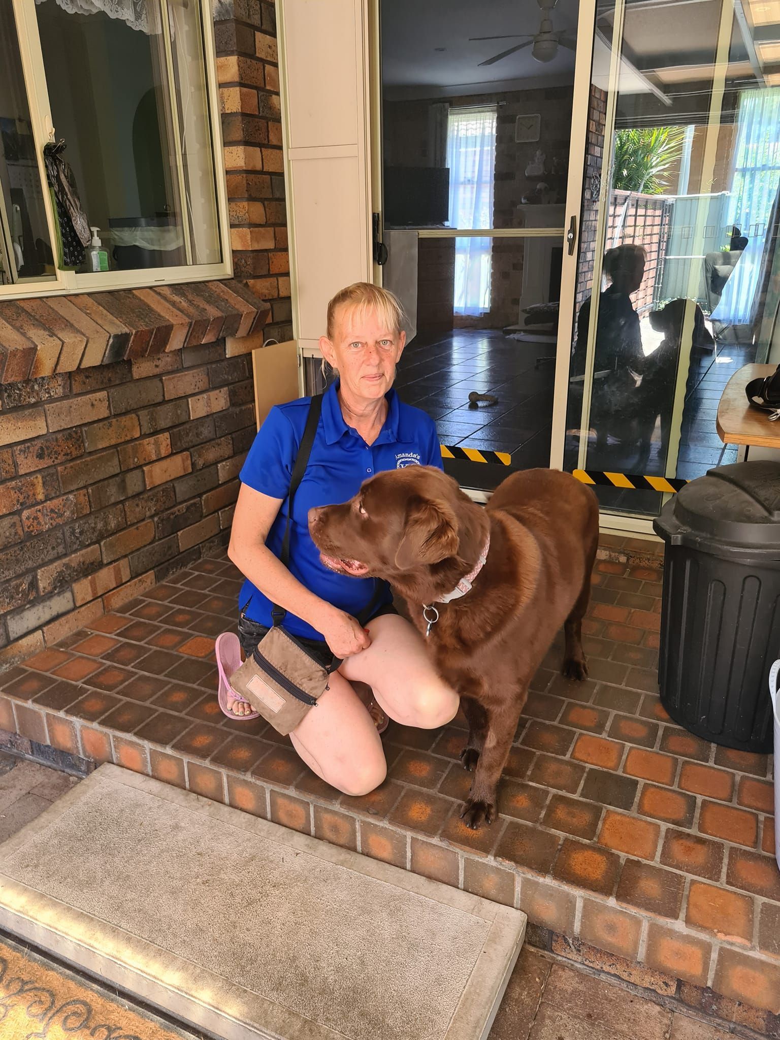 Woman Kneeling With a Brown Labrador Dog on a Brick Porch — Amanda's Professional K9 Training In Forster, NSW