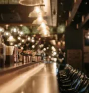 An empty bar counter with warm, glowing pendant lights, wood surfaces, and a row of dark stools in a dim, upscale setting.