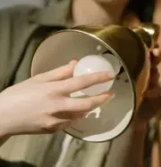 Close-up of a person holding a small, round lightbulb inside a gold-colored metal lamp shade.