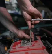 A mechanic uses a metal wrench and socket to work on a red car engine in a garage.