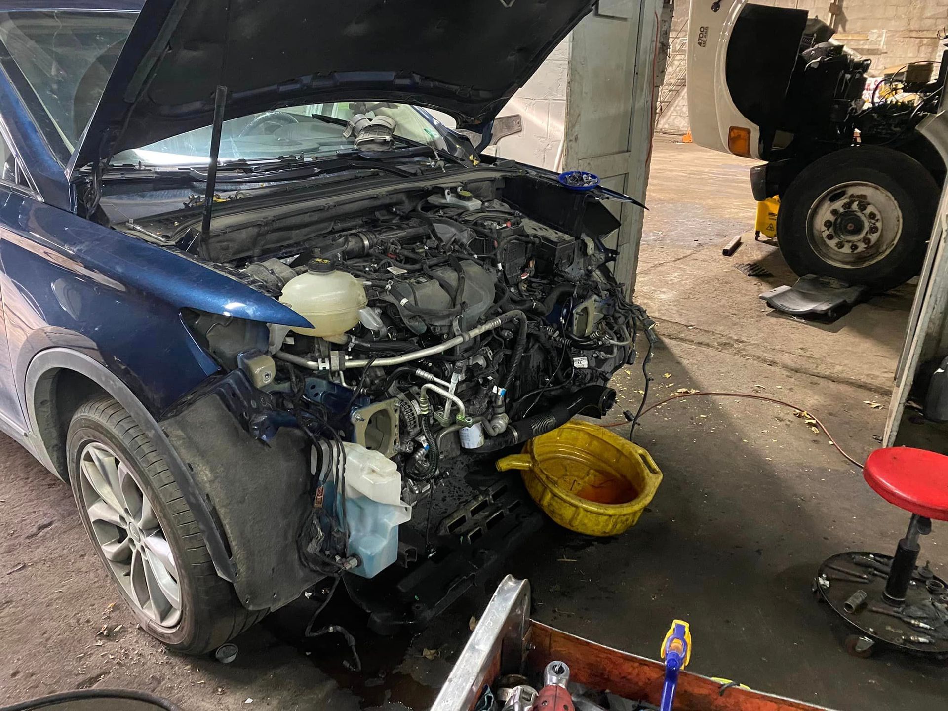 A blue car with the hood up is being worked on in a garage.