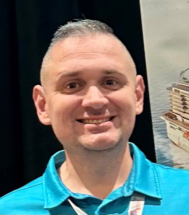 Man with shaved sides smiling, wearing a blue shirt.