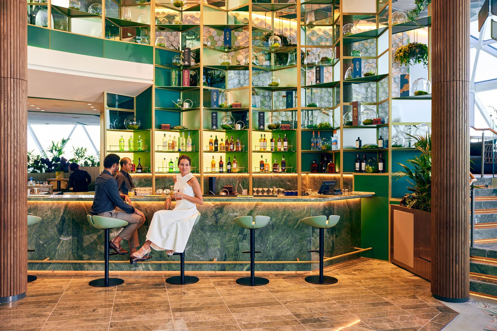 Bar with green accents, shelves of liquor, and patrons seated on stools.