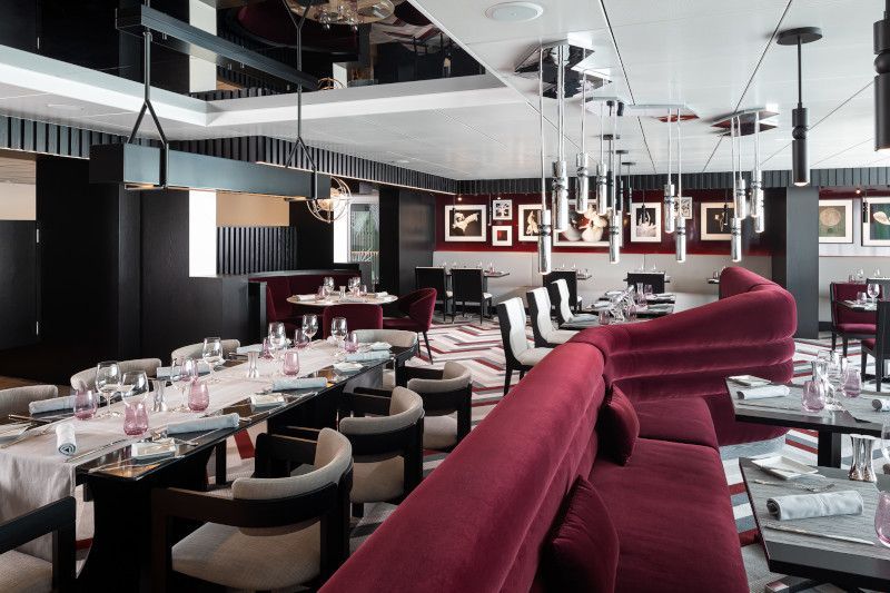 Upscale restaurant interior with red velvet booth seating, tables set with glassware, and modern lighting.