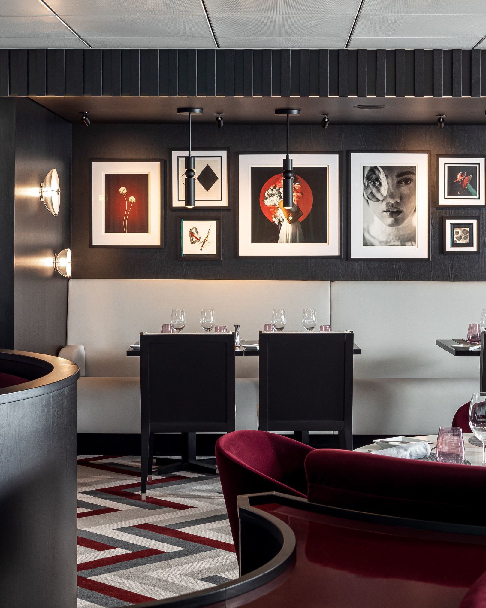 Restaurant interior with framed art on dark wall, booth seating, black chairs, patterned floor.