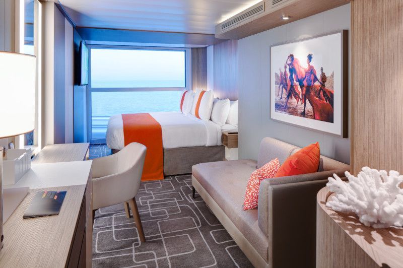 Cruise ship stateroom interior with a bed, sofa, desk, and ocean view.