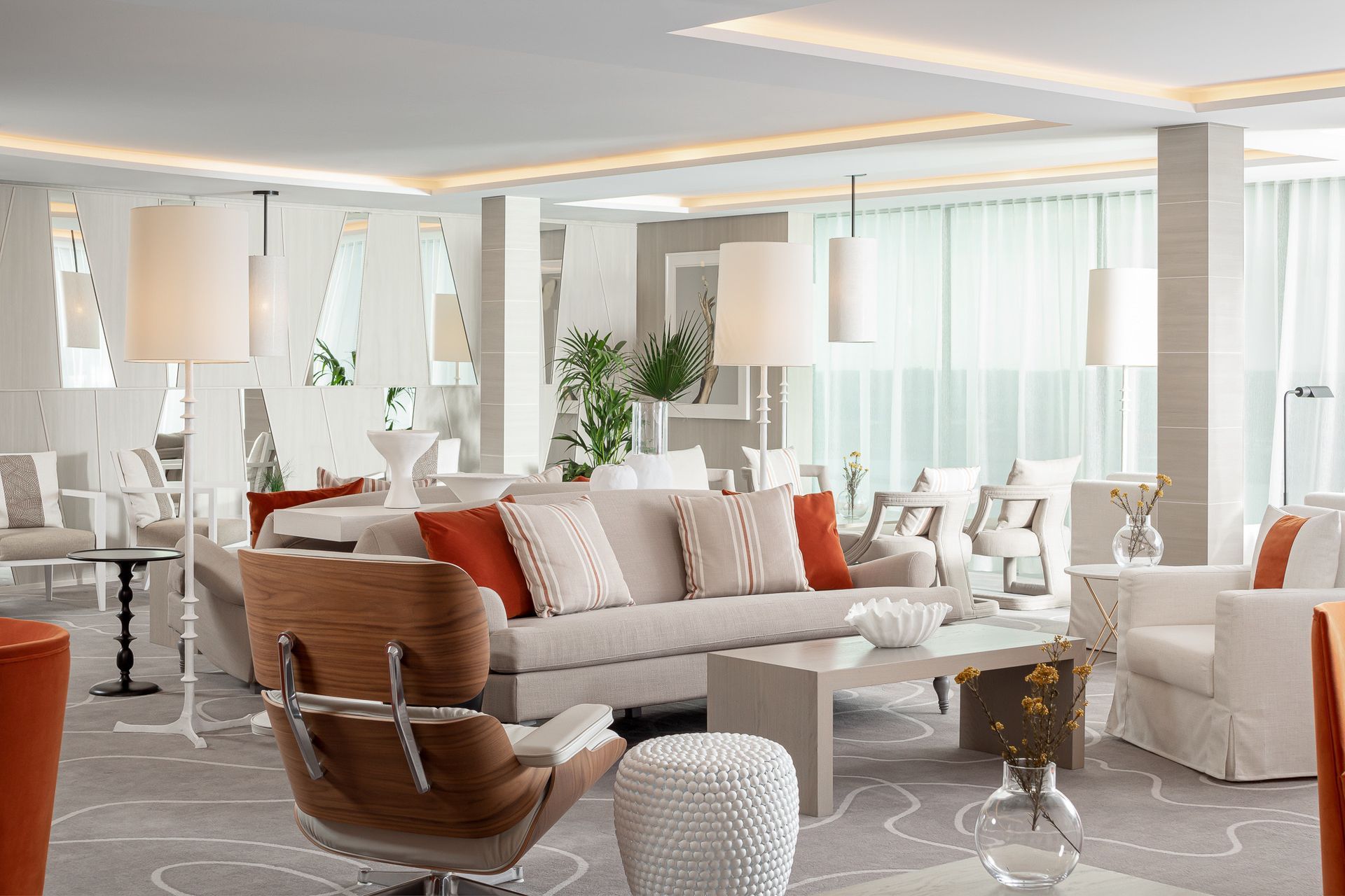 Bright, modern hotel lounge with neutral colors, couches, chairs, and lamps. Orange accents.