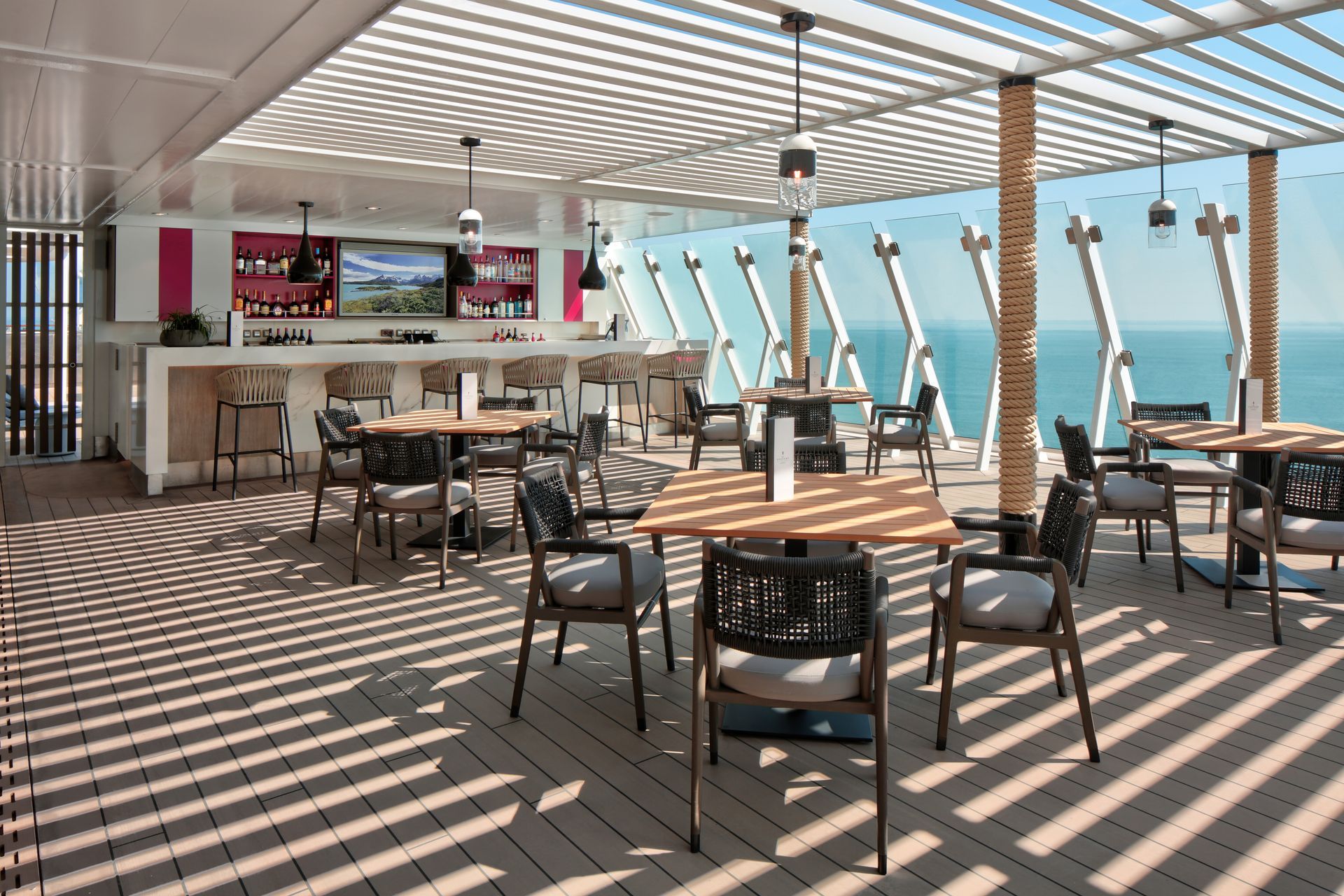 Outdoor bar with tables and chairs on a deck, with ocean view.
