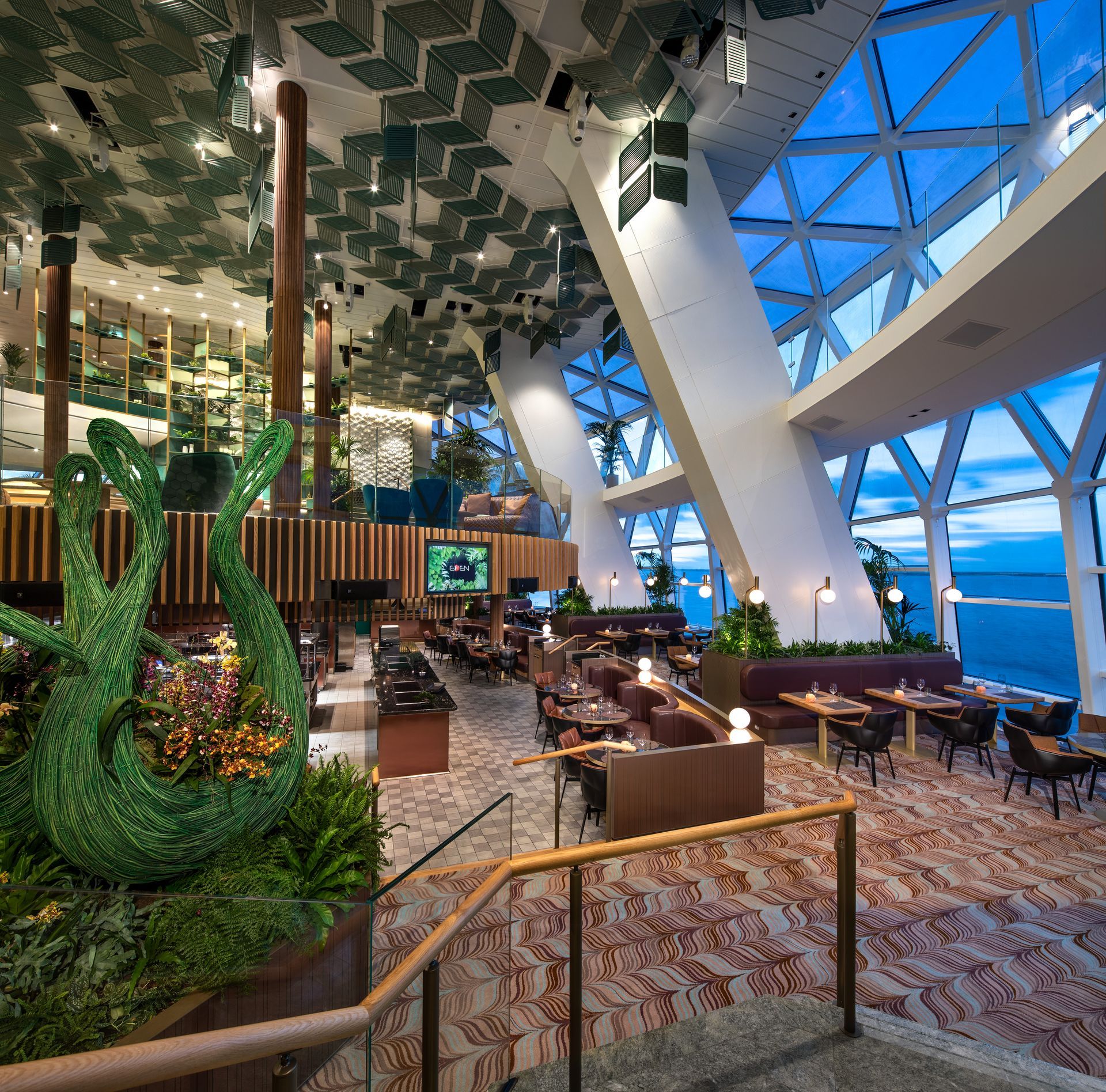 Interior of a modern restaurant with large windows, decorative ceiling, and views of the ocean.