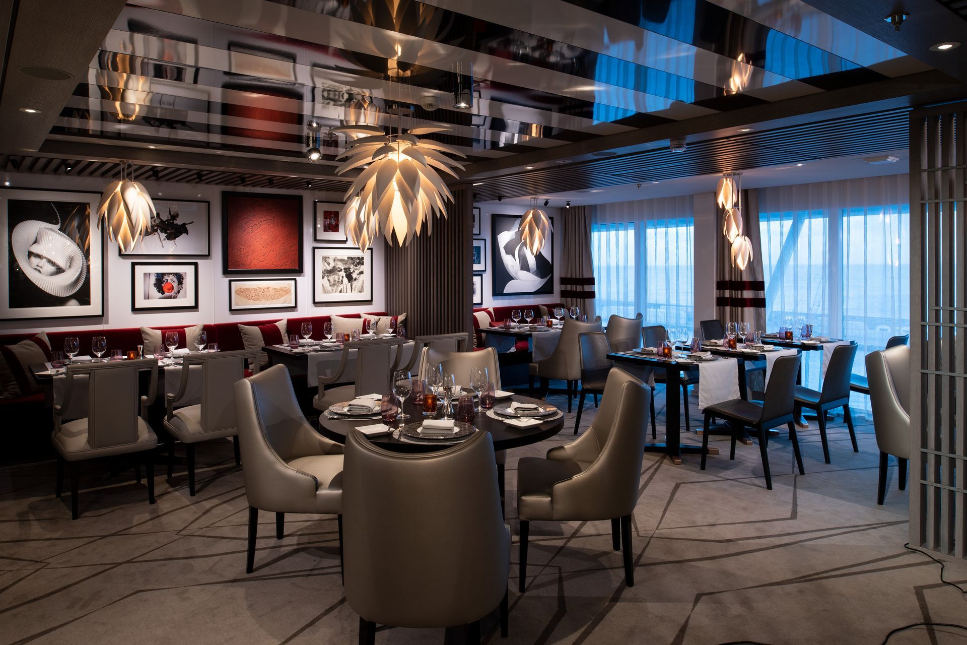 Upscale restaurant interior with tables, chairs, art, and pendant lights. A window overlooks a cityscape.