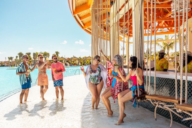  Guests socialize and enjoy cocktails at a swim-up bar in the Celebration Key Lagoon, featuring unique rope swing seats and shallow entry water.