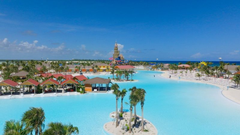 Tropical resort with light blue lagoon, palm trees, and structures under a bright blue sky.