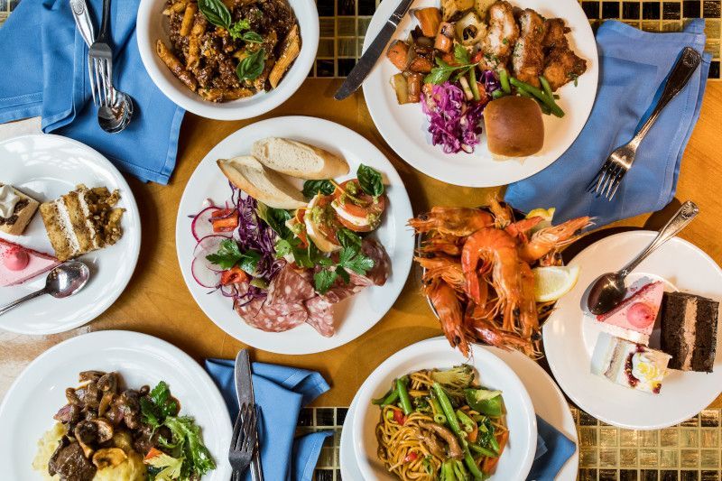 A buffet table with various dishes: pasta, meat, salad, shrimp, cake, and bread.