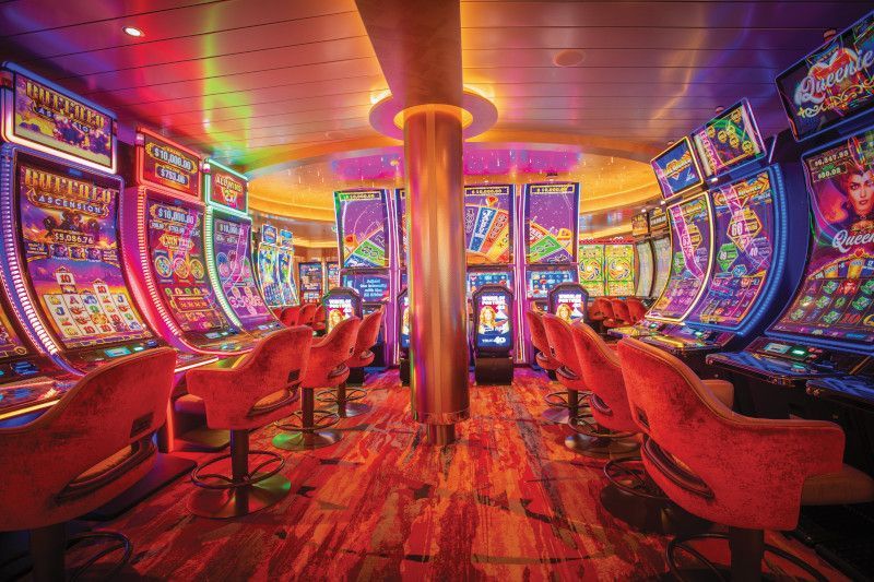 Slot machines in a brightly lit, colorful casino with red chairs.