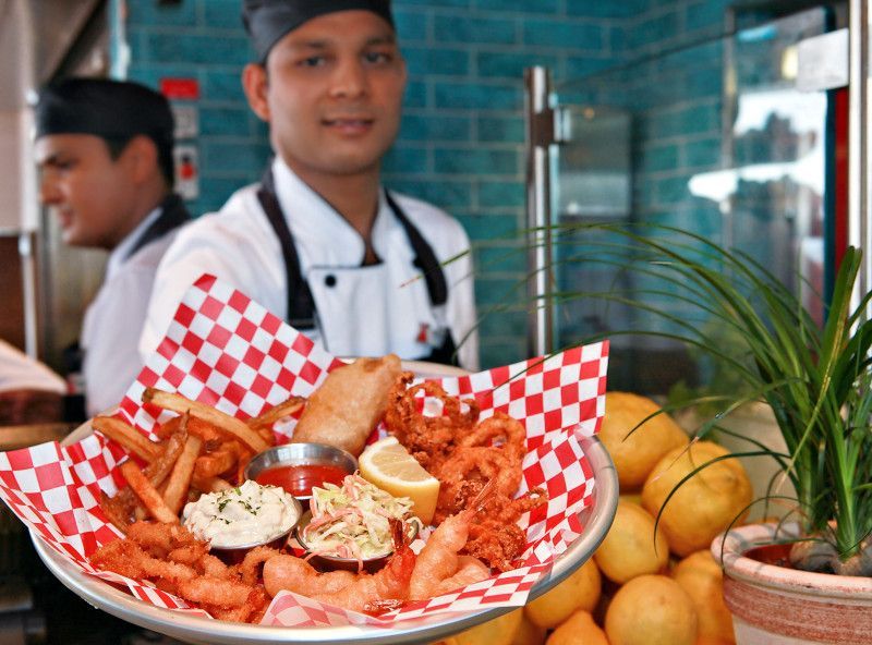 Chef holding a platter of fried seafood with fries and dipping sauces, in a restaurant.