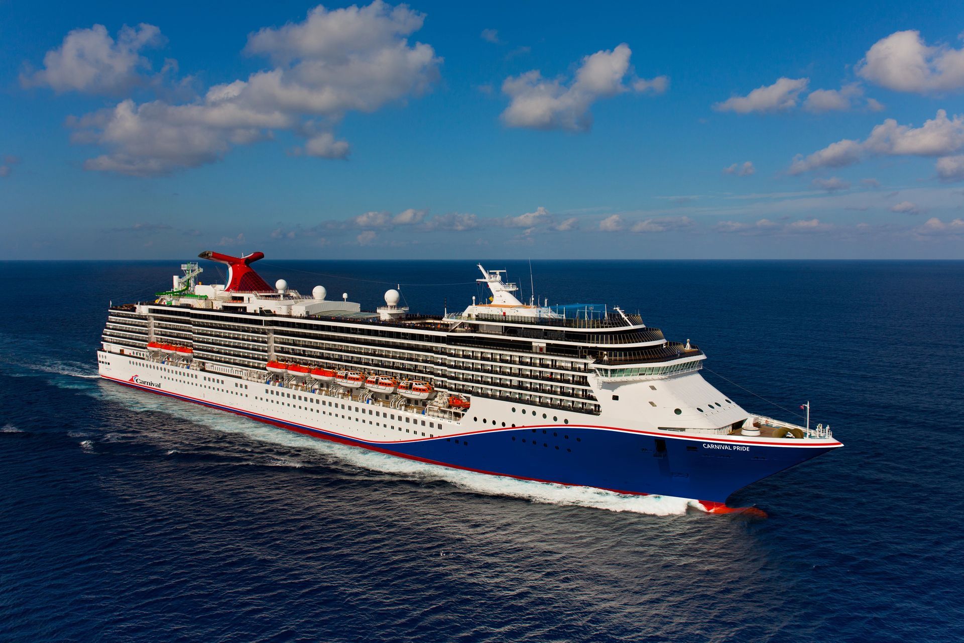 Large Carnival cruise ship sailing on a blue ocean under a partly cloudy sky.