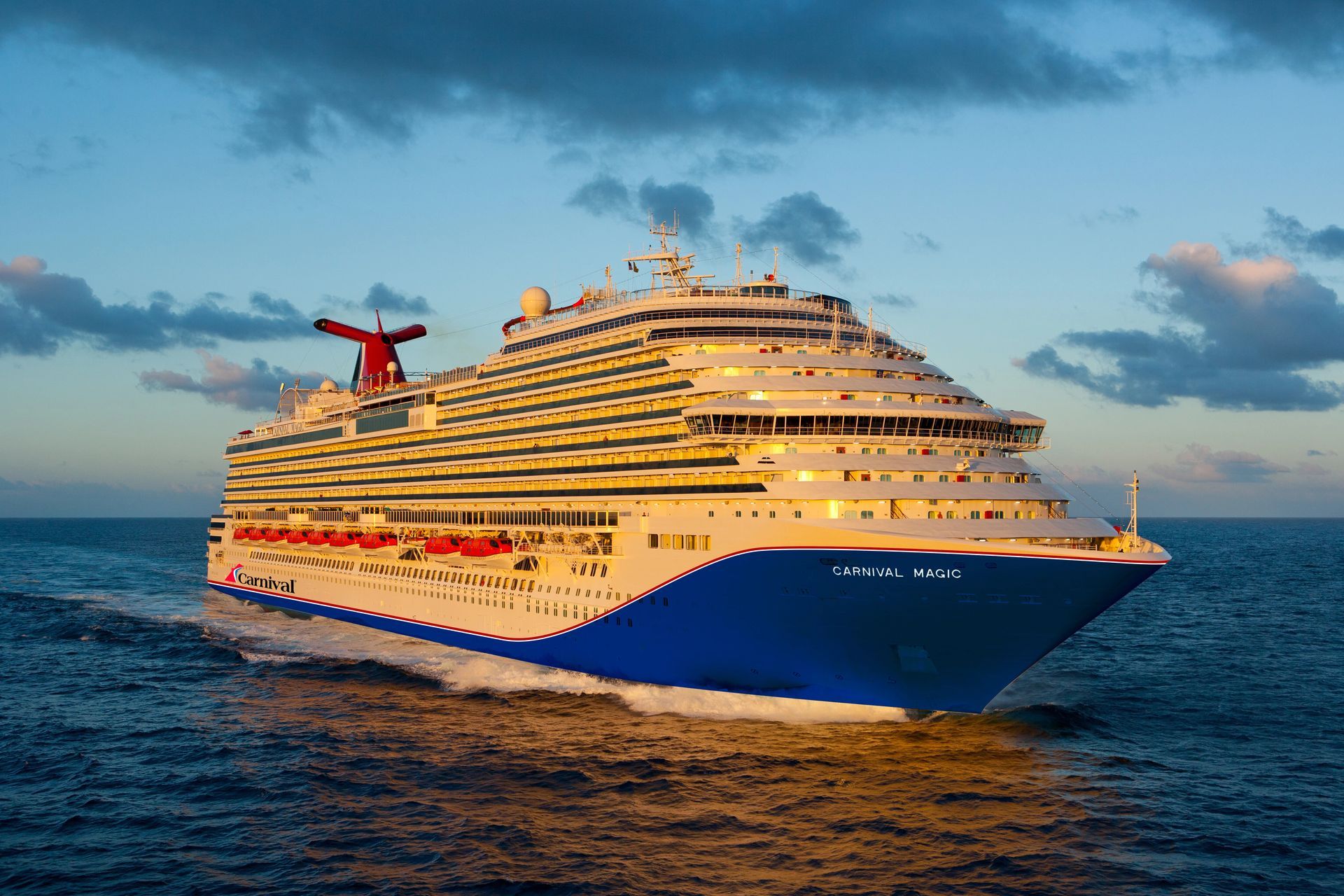 Carnival Magic with a blue bow, red stripe and white pain sailing on blue ocean under a cloudy sky.