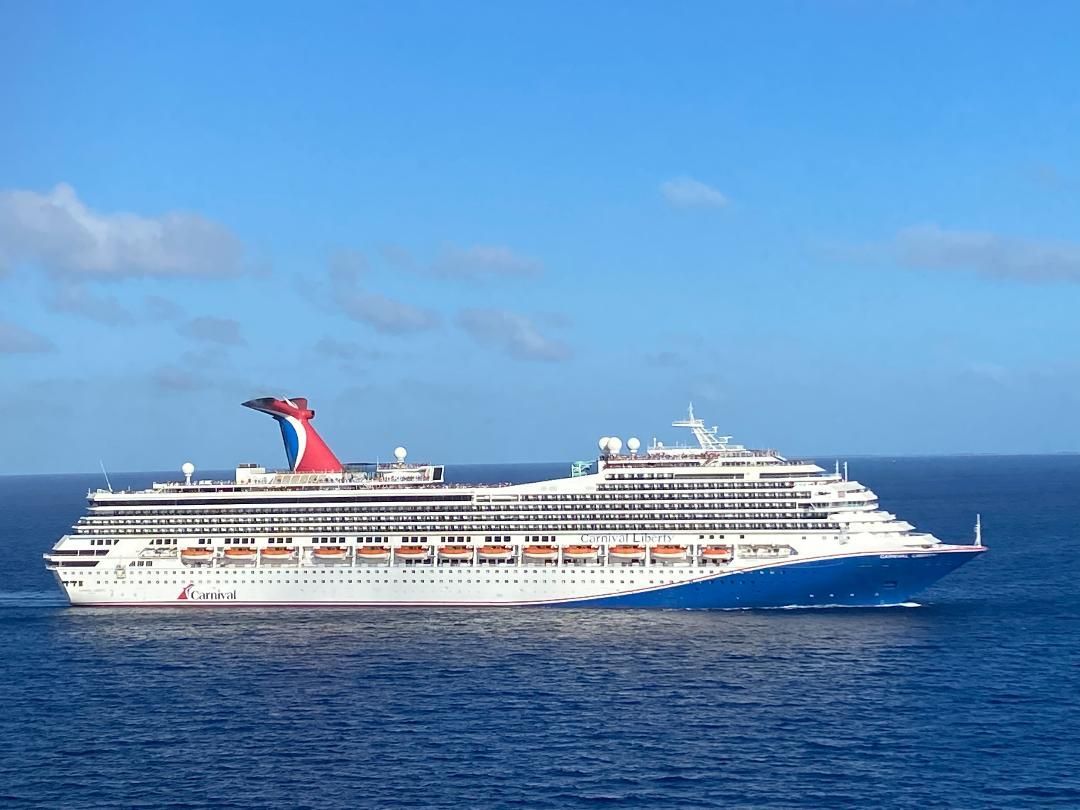 Cruise ship on the ocean with a blue hull, white superstructure, and a red, white, and blue funnel against a blue sky.