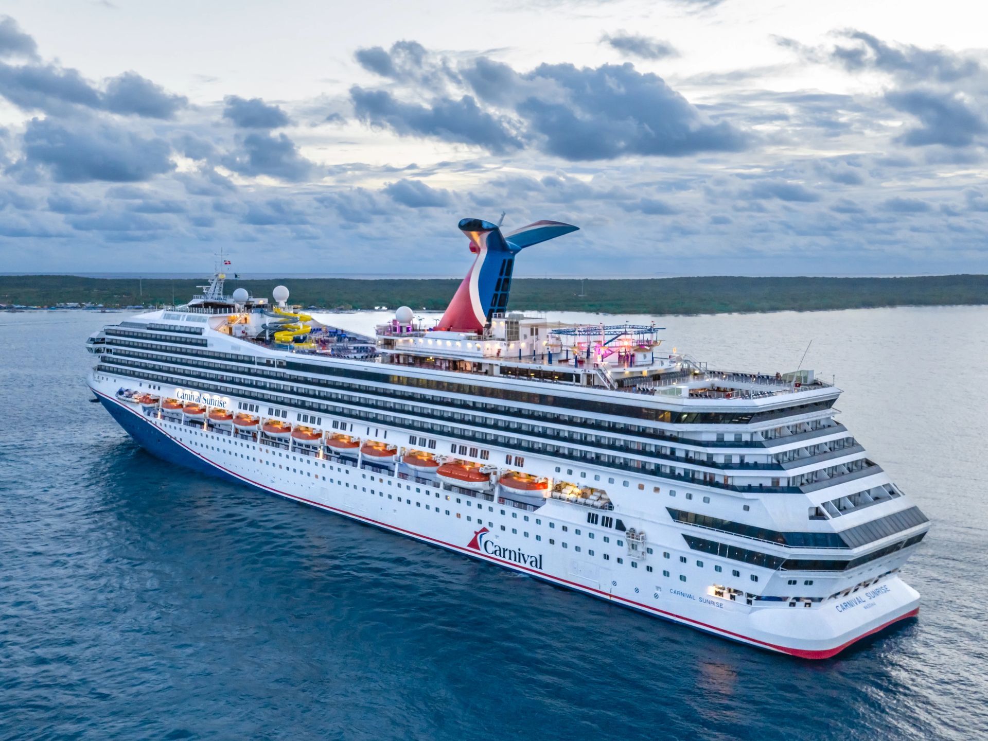 Large Carnival cruise ship sailing on blue water under a cloudy sky.