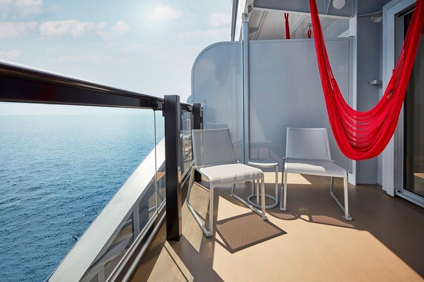 Private Sea Terrace balcony on Virgin Voyages featuring two modern chairs, a small table, and the line’s signature red hammock overlooking the open ocean.