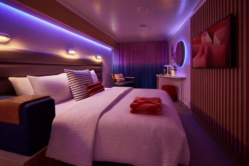 A modern bedroom with purple and blue lighting, a bed, and artwork.