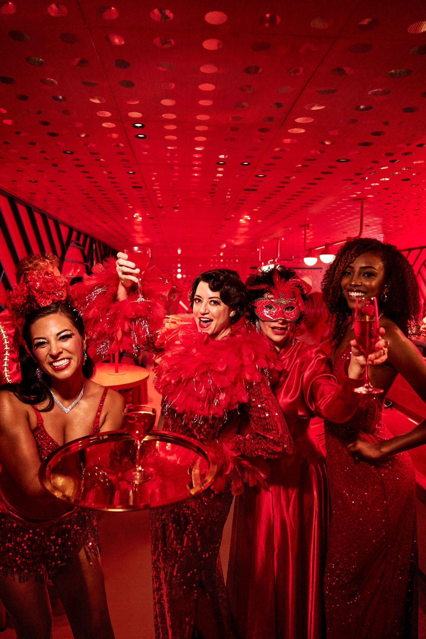 Guests dressed in glamorous red attire celebrate with cocktails inside a vividly lit red lounge on a Virgin Voyages ship, capturing the line’s vibrant adults-only nightlife and festive onboard atmosphere.