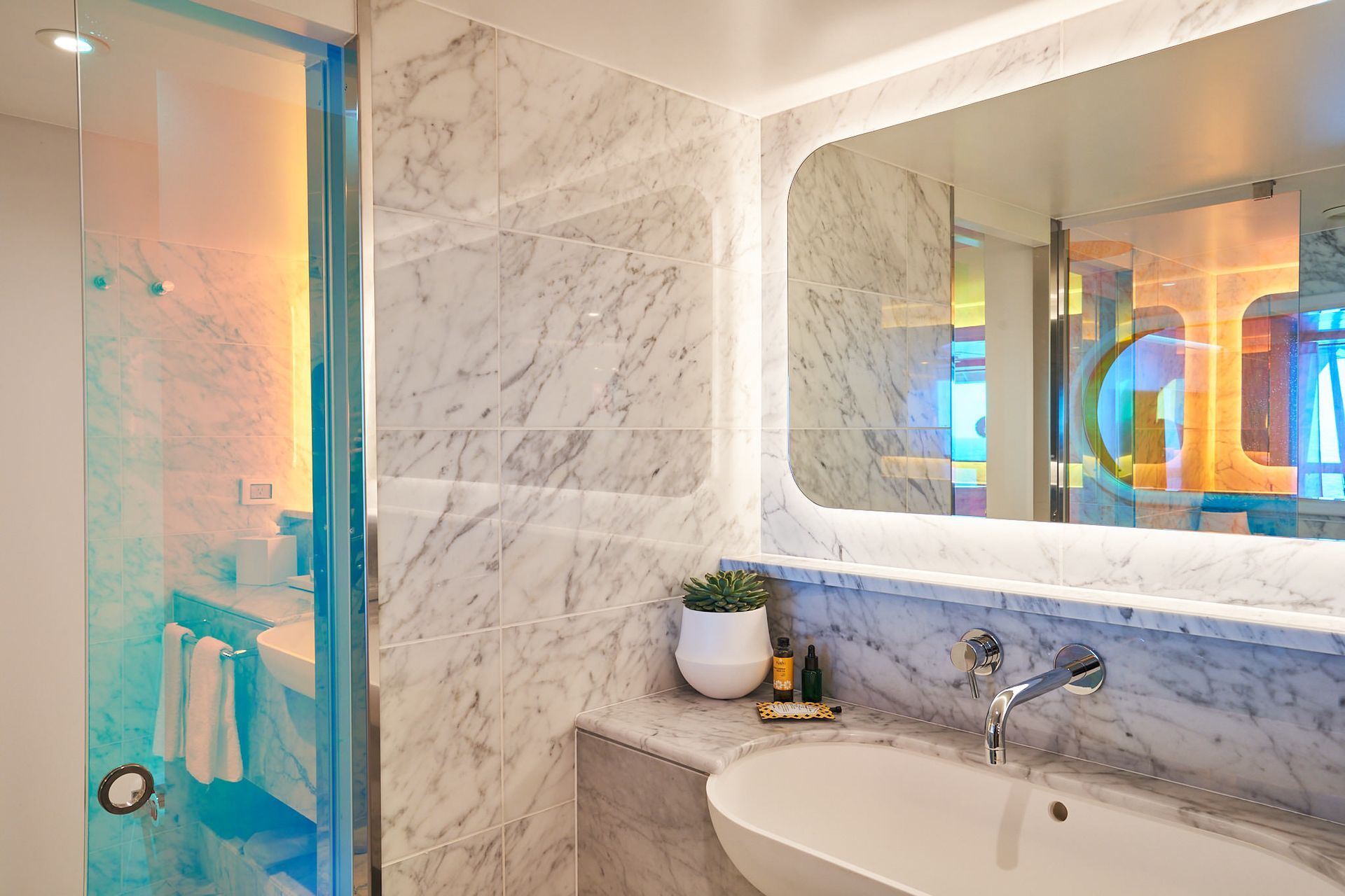 Bathroom with marble walls, large mirror, and a colorful glass shower.