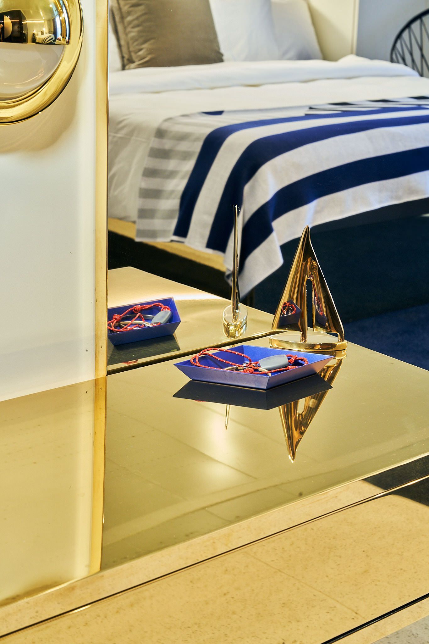 Reflective table with nautical decor and a bed with blue and white striped blanket in the background.