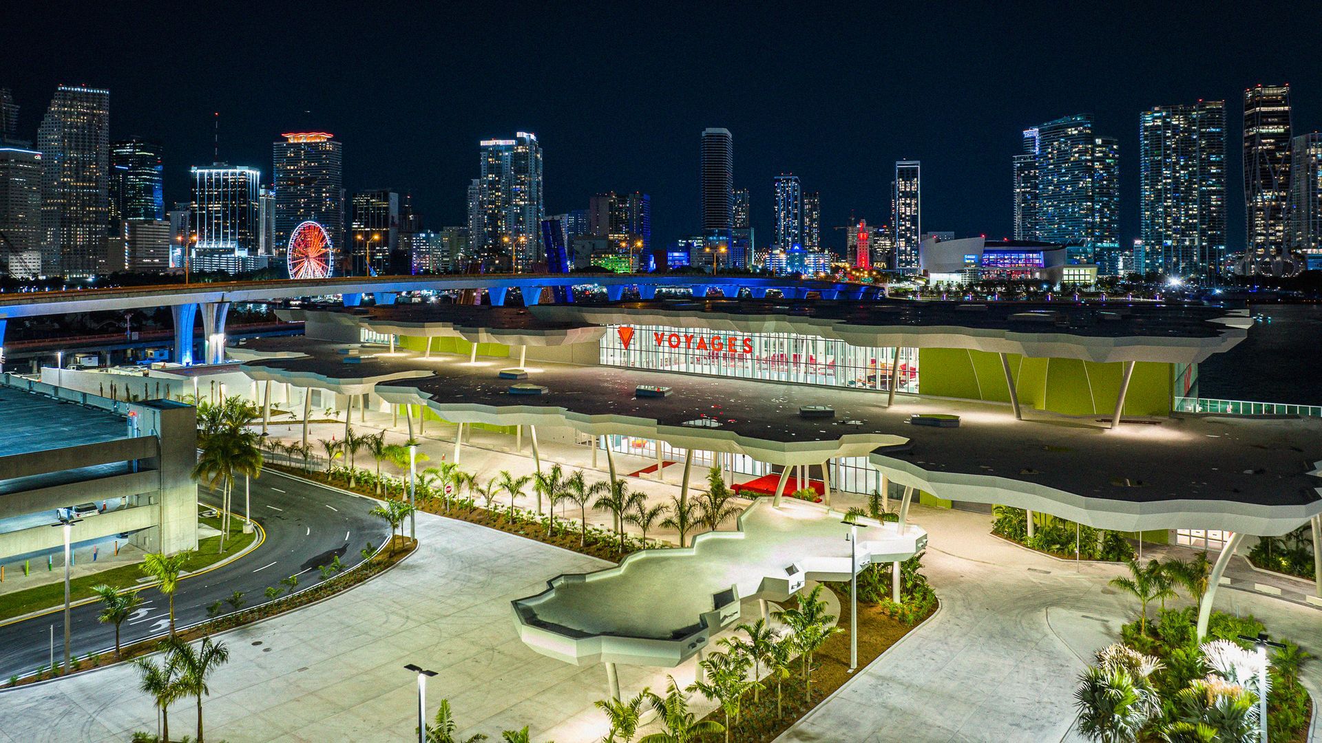 Nighttime view of Virgin Voyages’ terminal at PortMiami, illuminated against the Miami skyline with palm trees and modern architecture showcasing the cruise line’s sleek, contemporary style.
