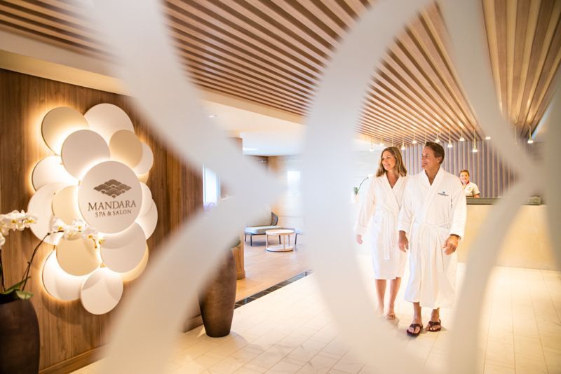 Couple in white robes walk through spa entrance, logo visible.