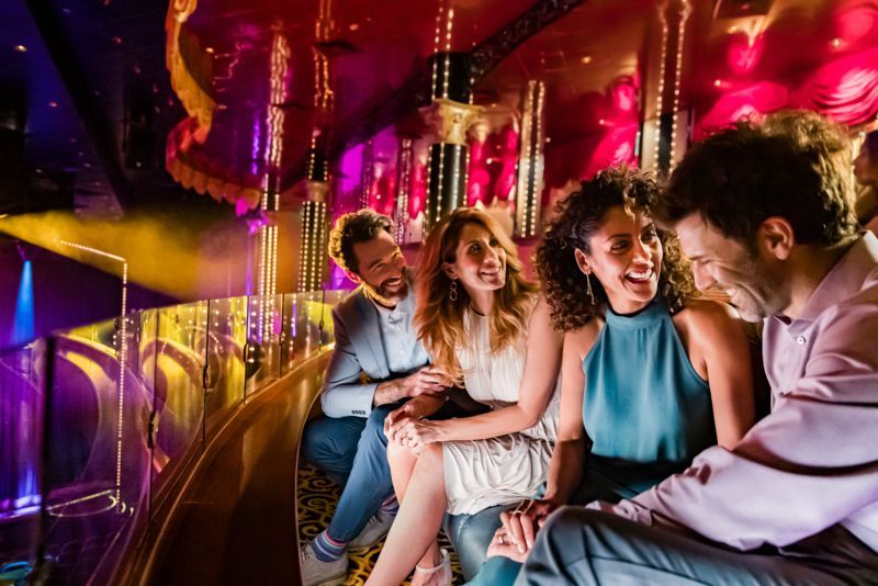 Four friends laughing together in a brightly lit, ornate setting, possibly a ride or show.