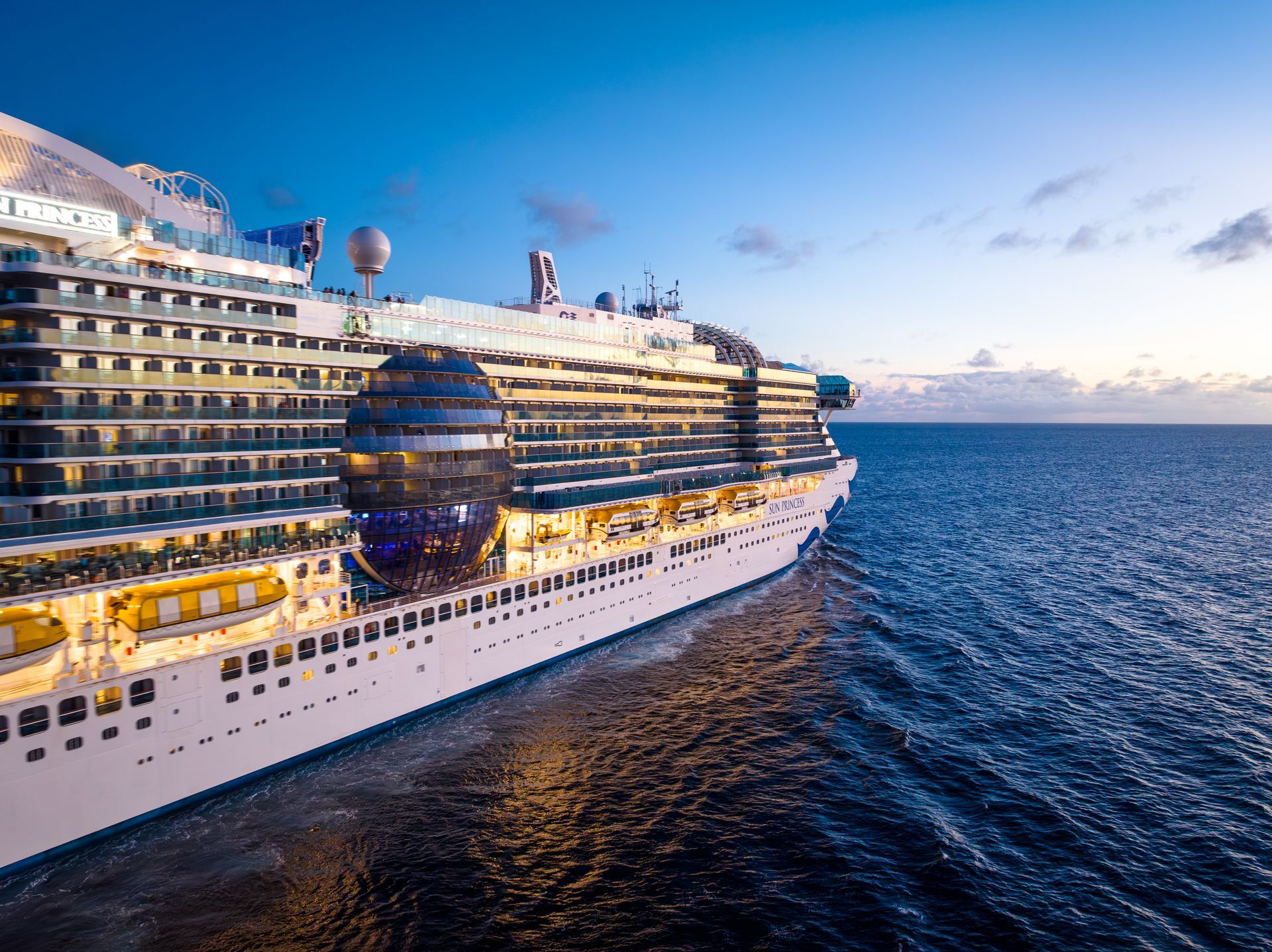 Cruise ship sailing on a blue ocean under a partly cloudy sky.