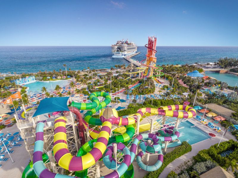 Water park with colorful slides and a cruise ship docked in the background on a sunny day.