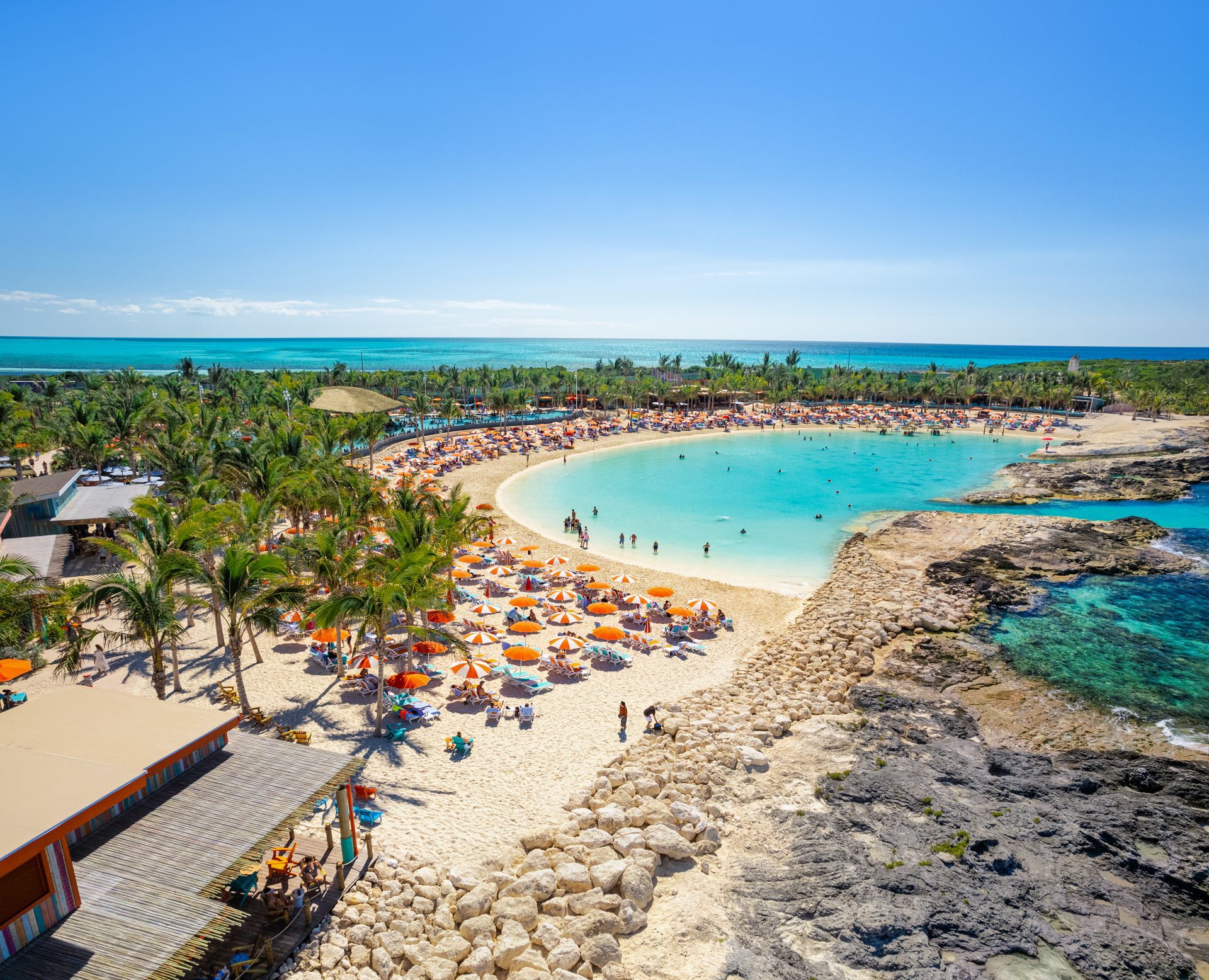 A tropical beach with turquoise water, palm trees, and many people enjoying the sun and swimming.