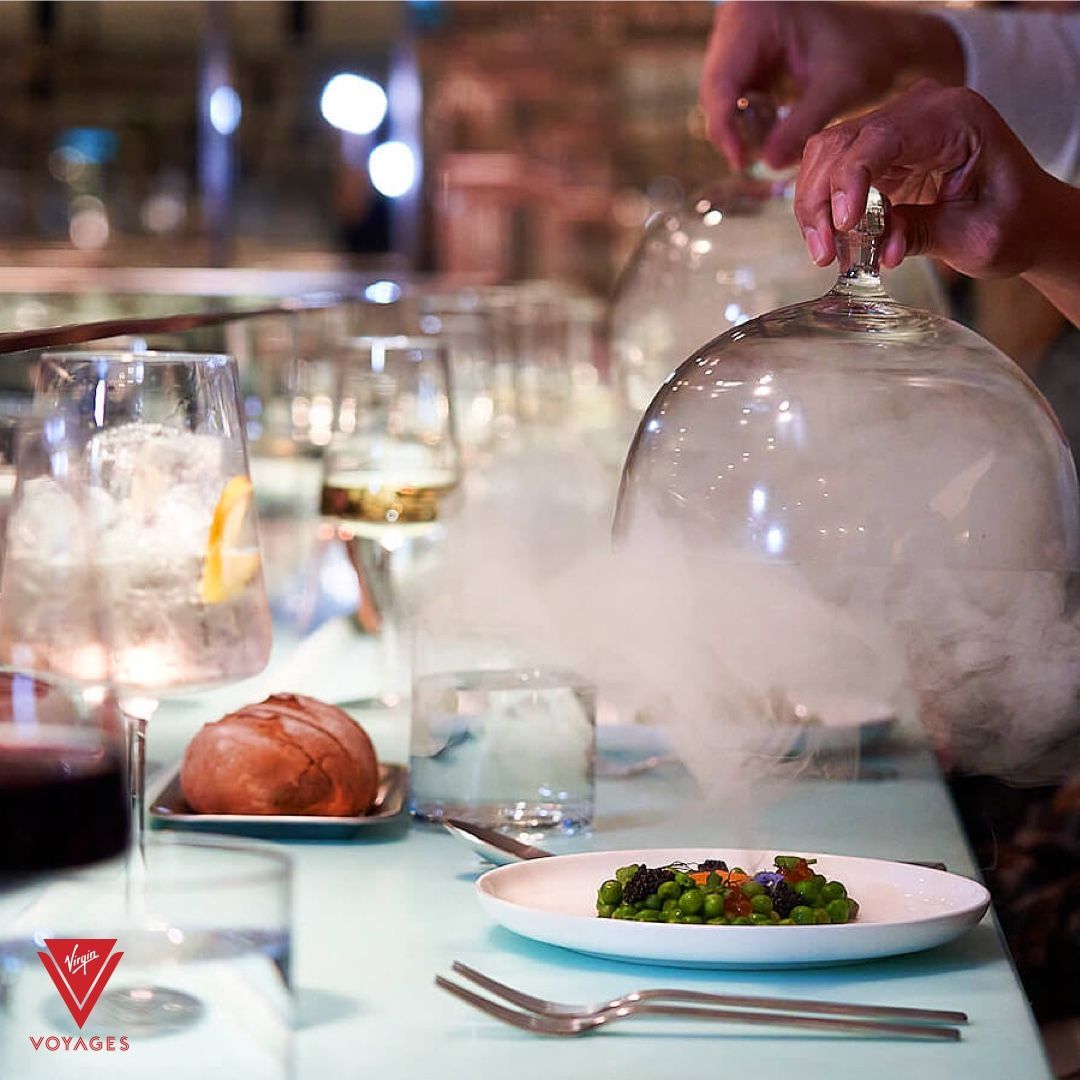 Close-up of a dish being revealed with smoke at a restaurant table setting at The Test Kitchen - Virgin Voyages Experimental, chef-led tasting lab serving inventive, multi-course dishes.