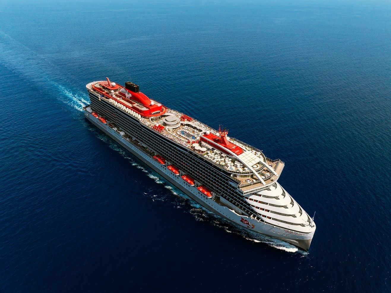 A large cruise ship sails across the blue water of the North Atlantic Ocean, leaving a white wake.