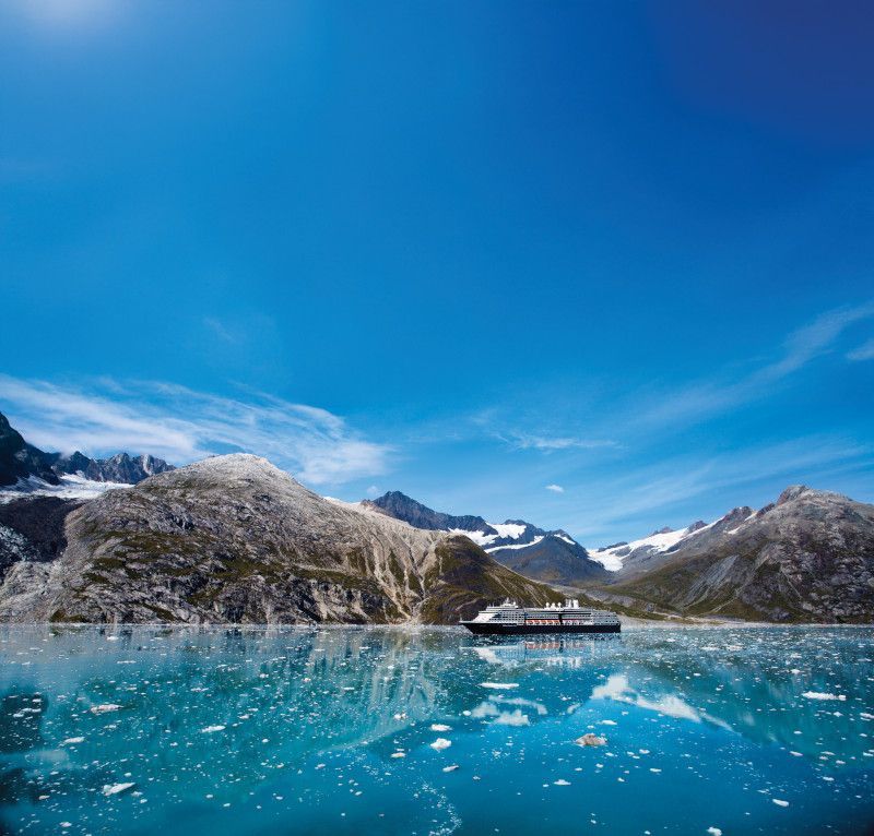 Cruise ship sailing on blue water near rocky mountains under a blue sky.