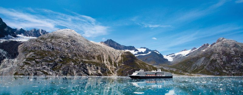 Cruise ship sails in turquoise water near mountains under a clear blue sky.