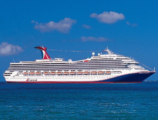 Large cruise ship sailing on blue water under a clear sky. Red, white, and blue color scheme.