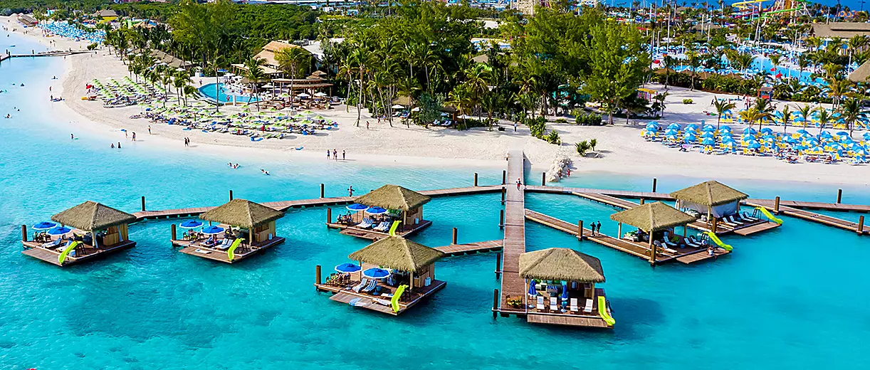 Overwater bungalows on turquoise water near a white sand beach and lush green trees.