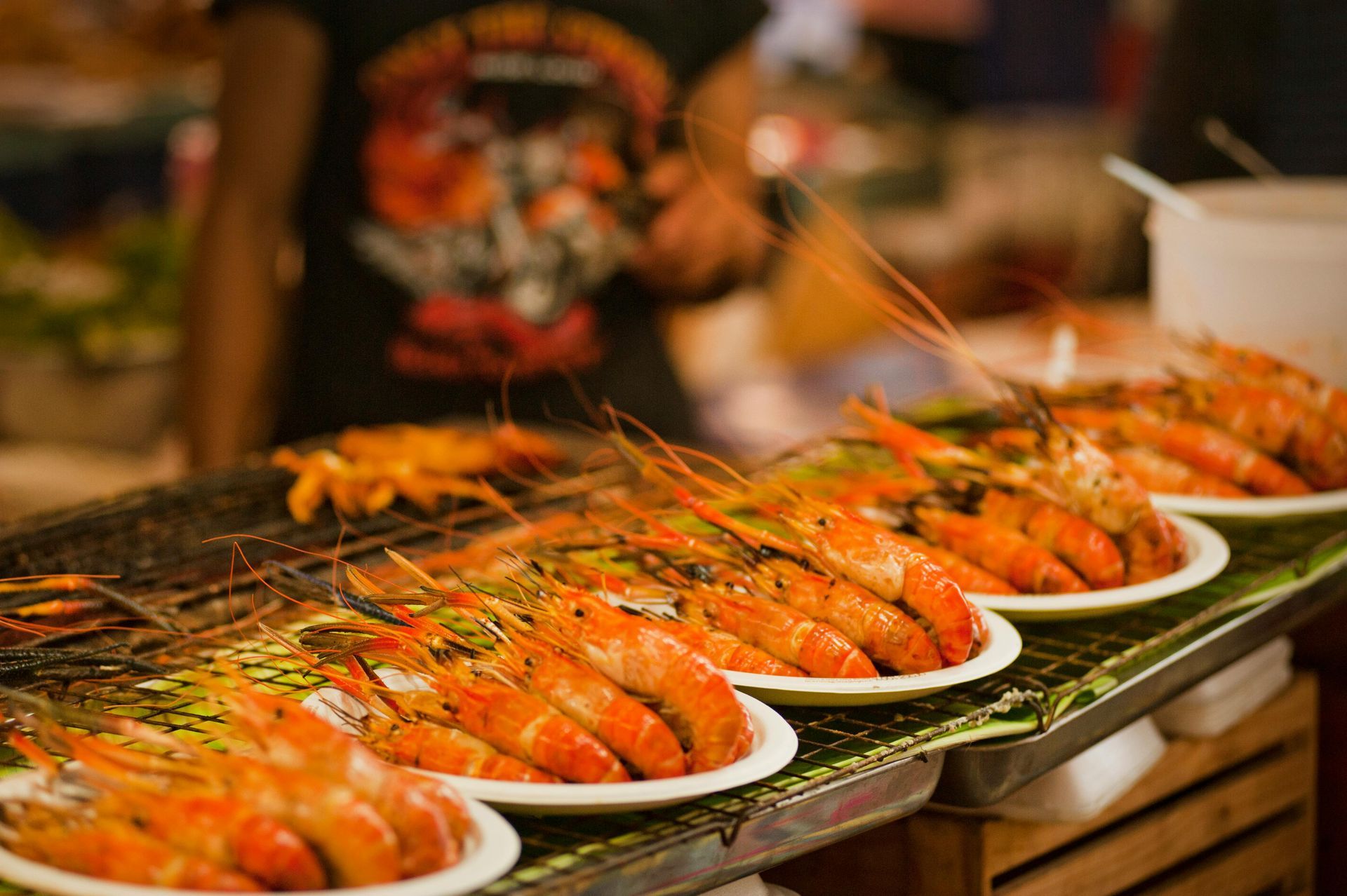 Grilled shrimp on plates at a food stall, person in background.