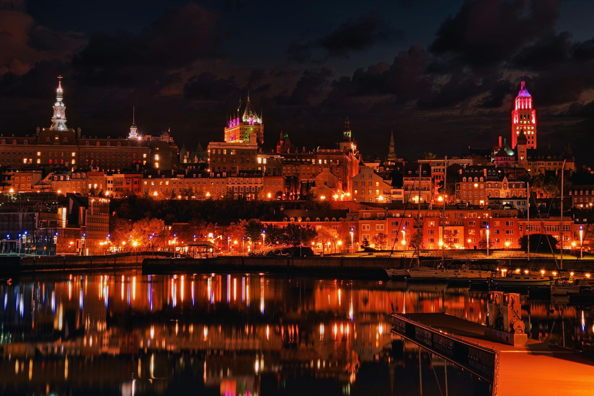 Nighttime cityscape reflects in water; buildings lit in orange and pink.