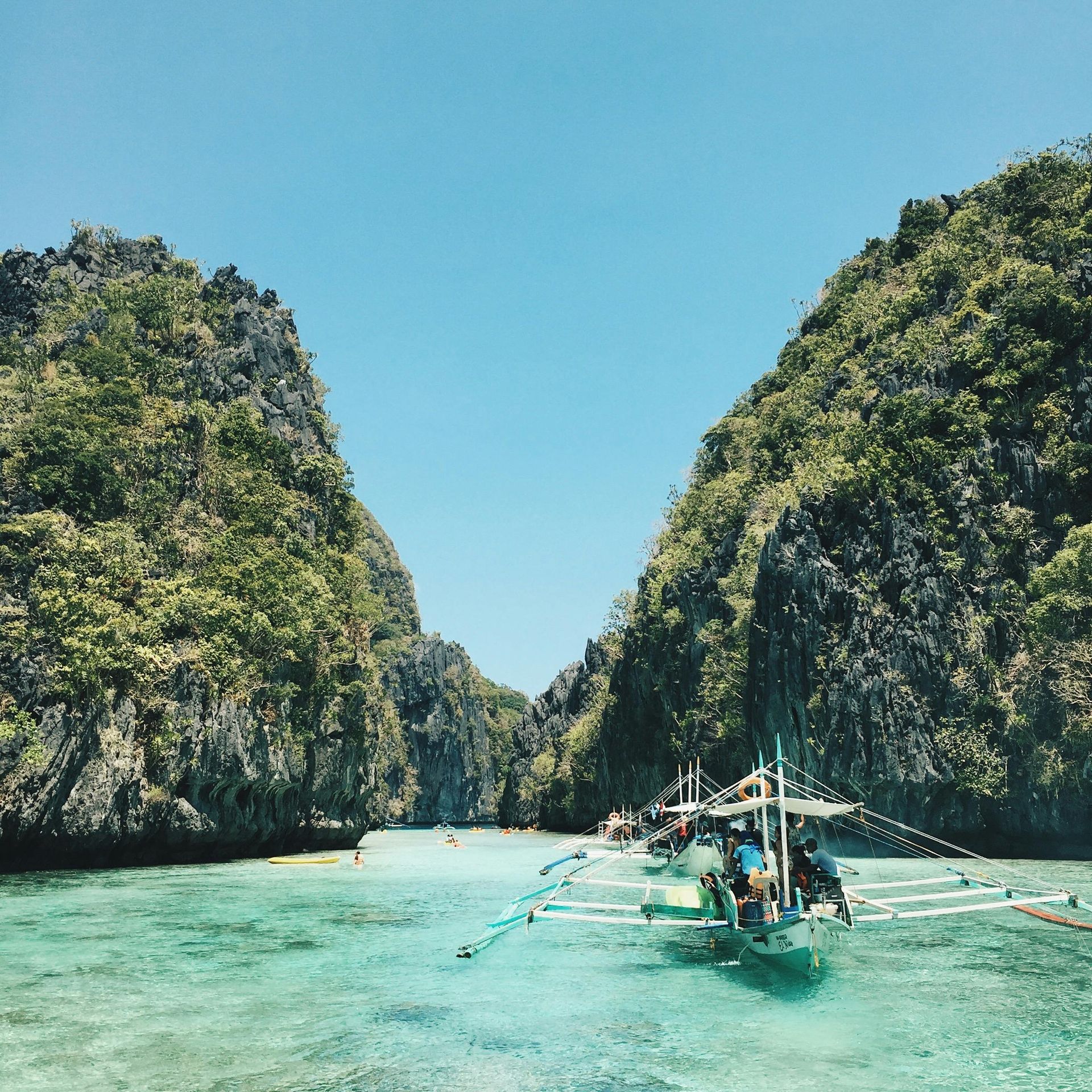 Boats in turquoise water between lush green cliffs under a bright blue sky.