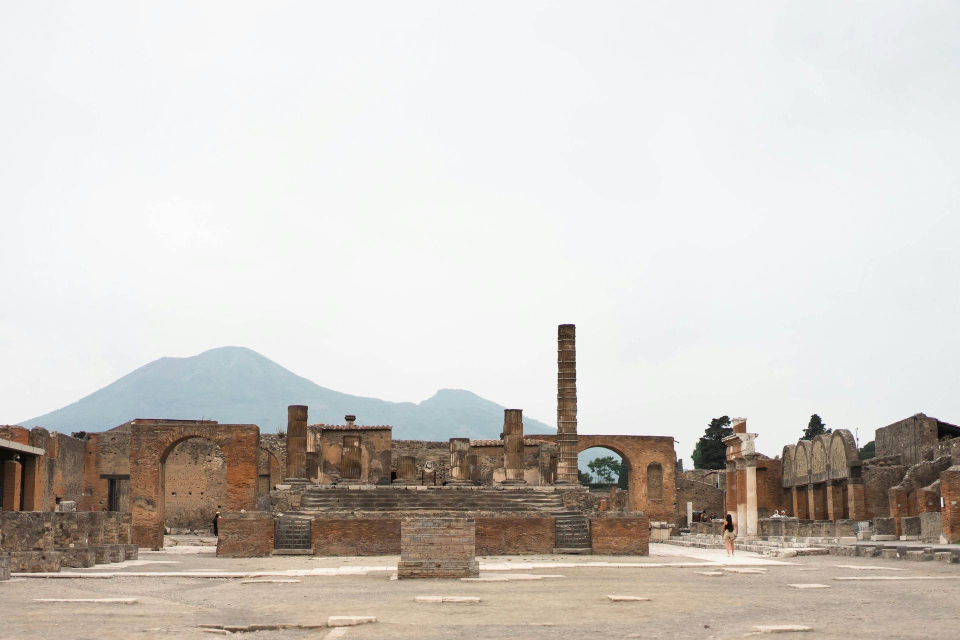 Ruins of Pompeii with Mount Vesuvius in the background, under an overcast sky.