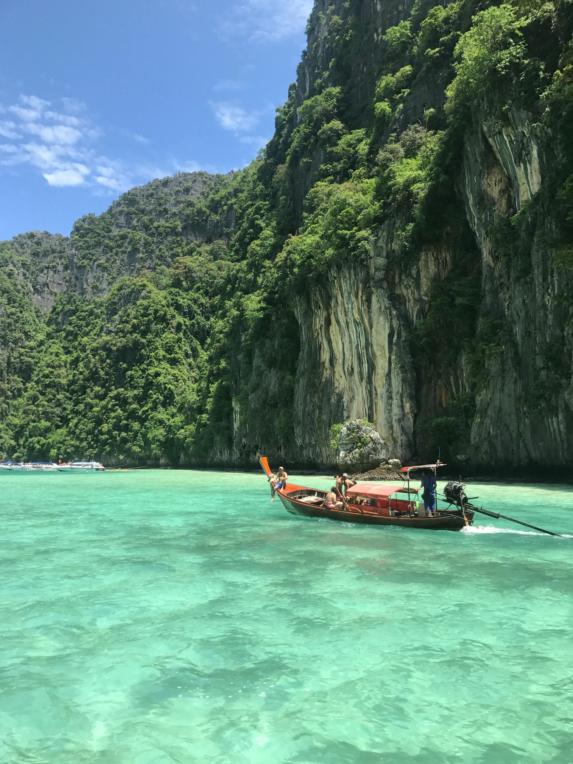 Boat on turquoise water near a lush, rocky cliff face. Bright sunny day.