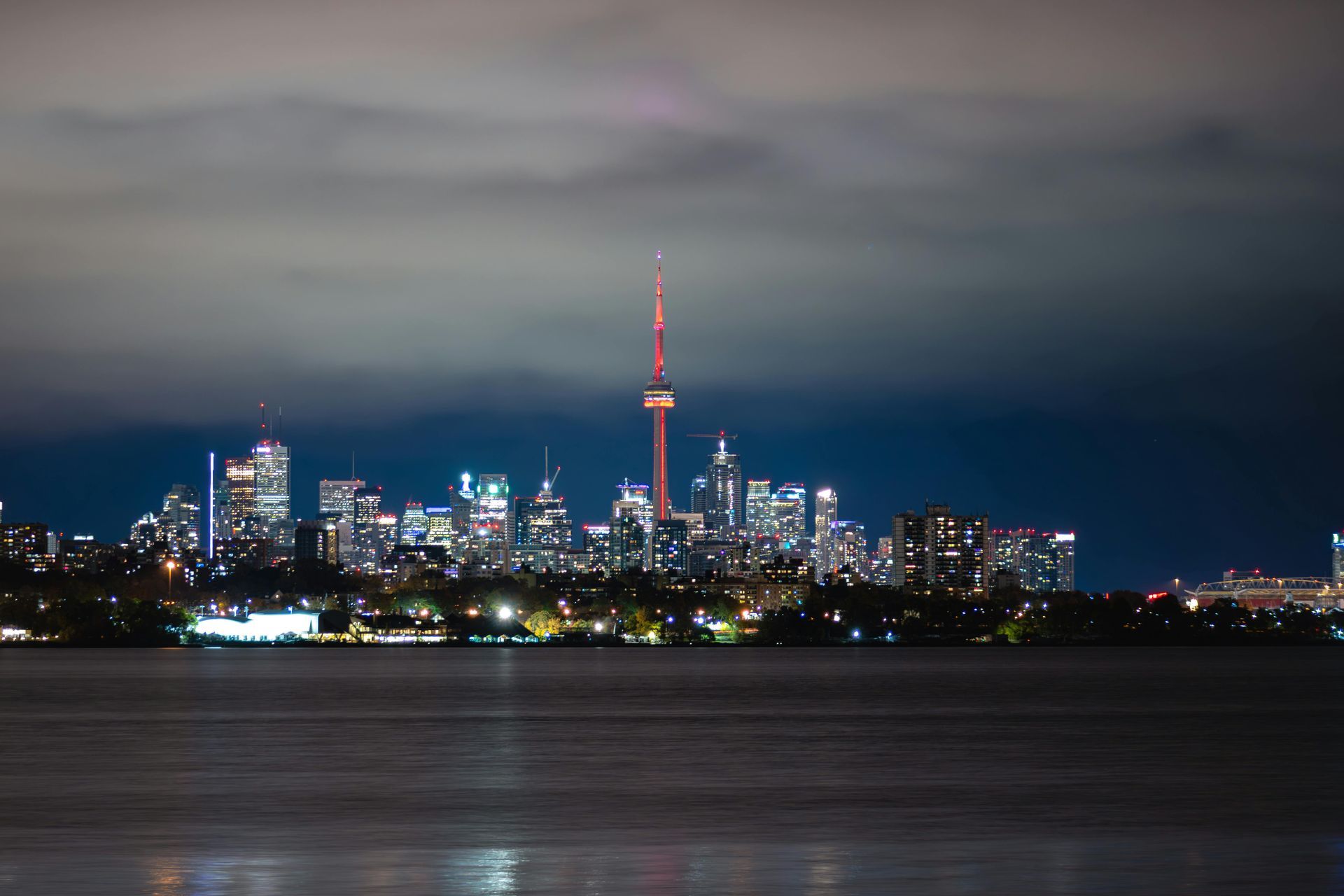 Nighttime skyline of Toronto, Canada, with the CN Tower prominently lit, viewed across dark water.