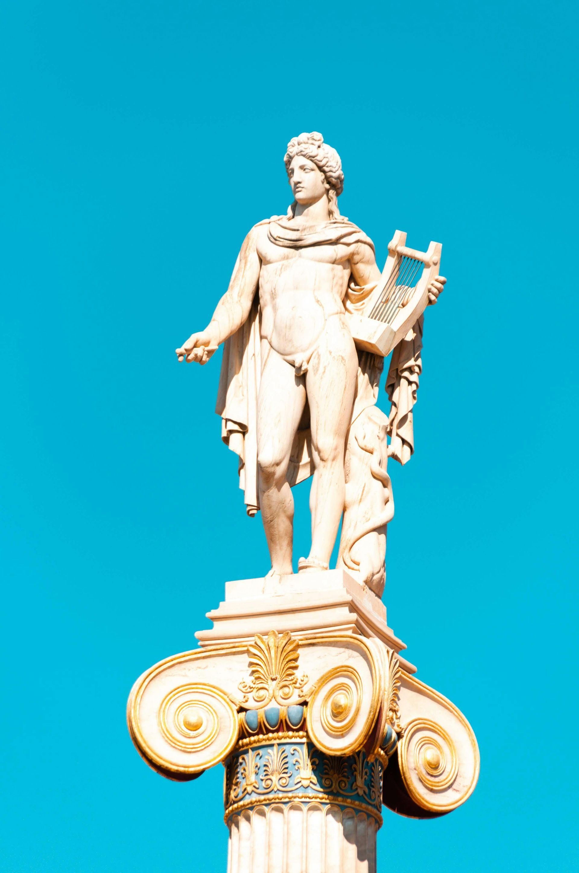 Statue of Apollo with lyre atop a Corinthian column against a bright blue sky.