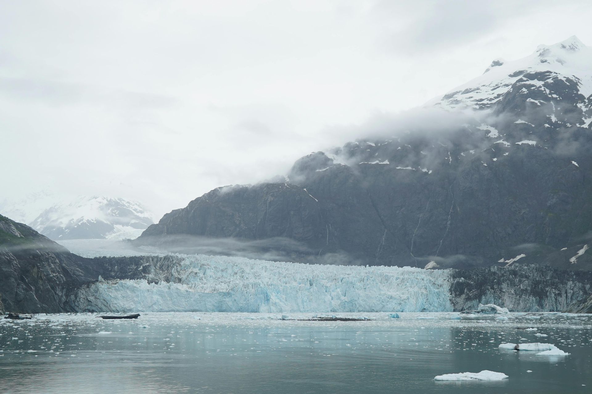 Glacier meets the sea, against a mountain backdrop under overcast skies. A view of Glacier Bay, Alaska
