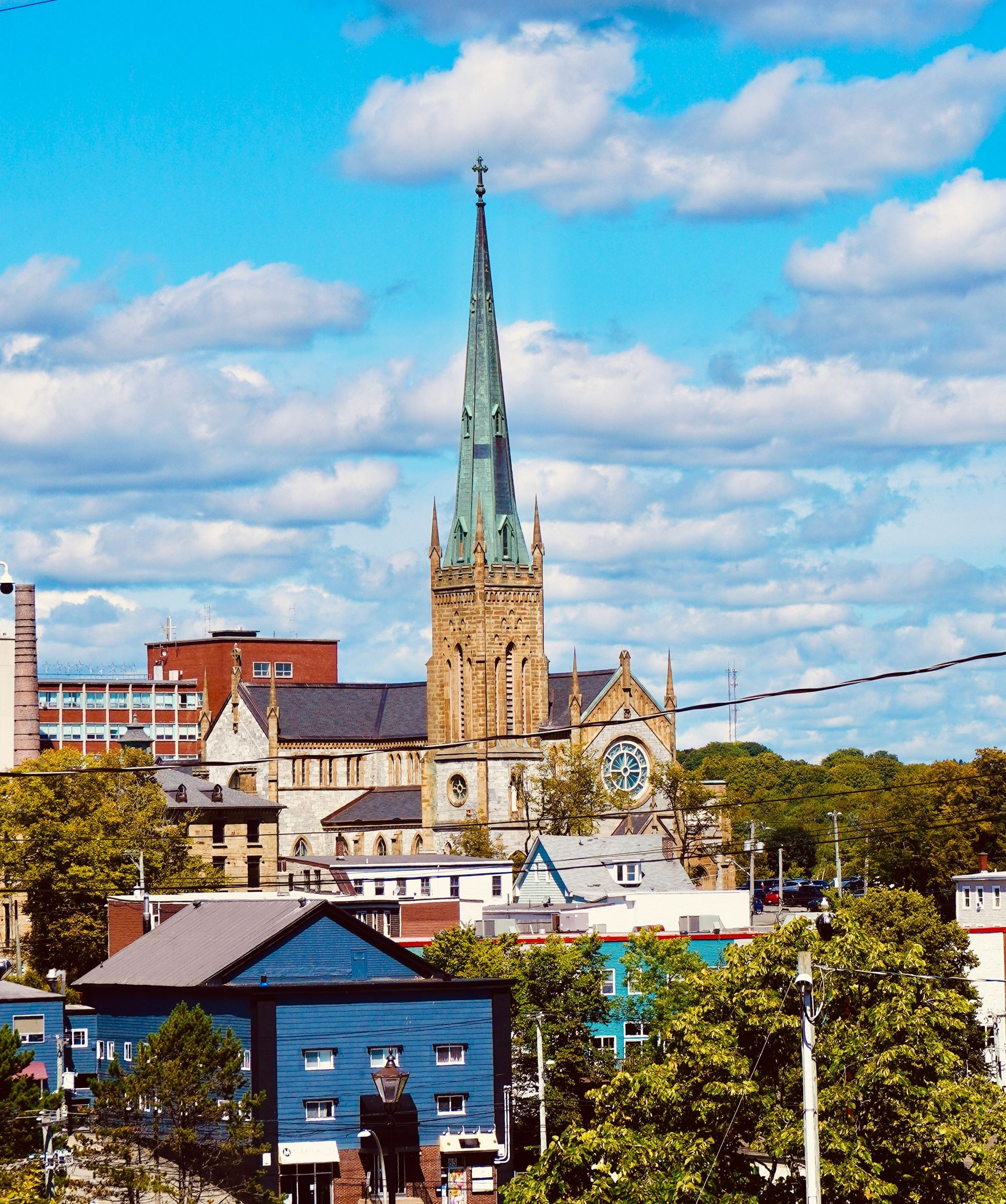 Church steeple rises above colorful buildings and trees under a cloudy blue sky.