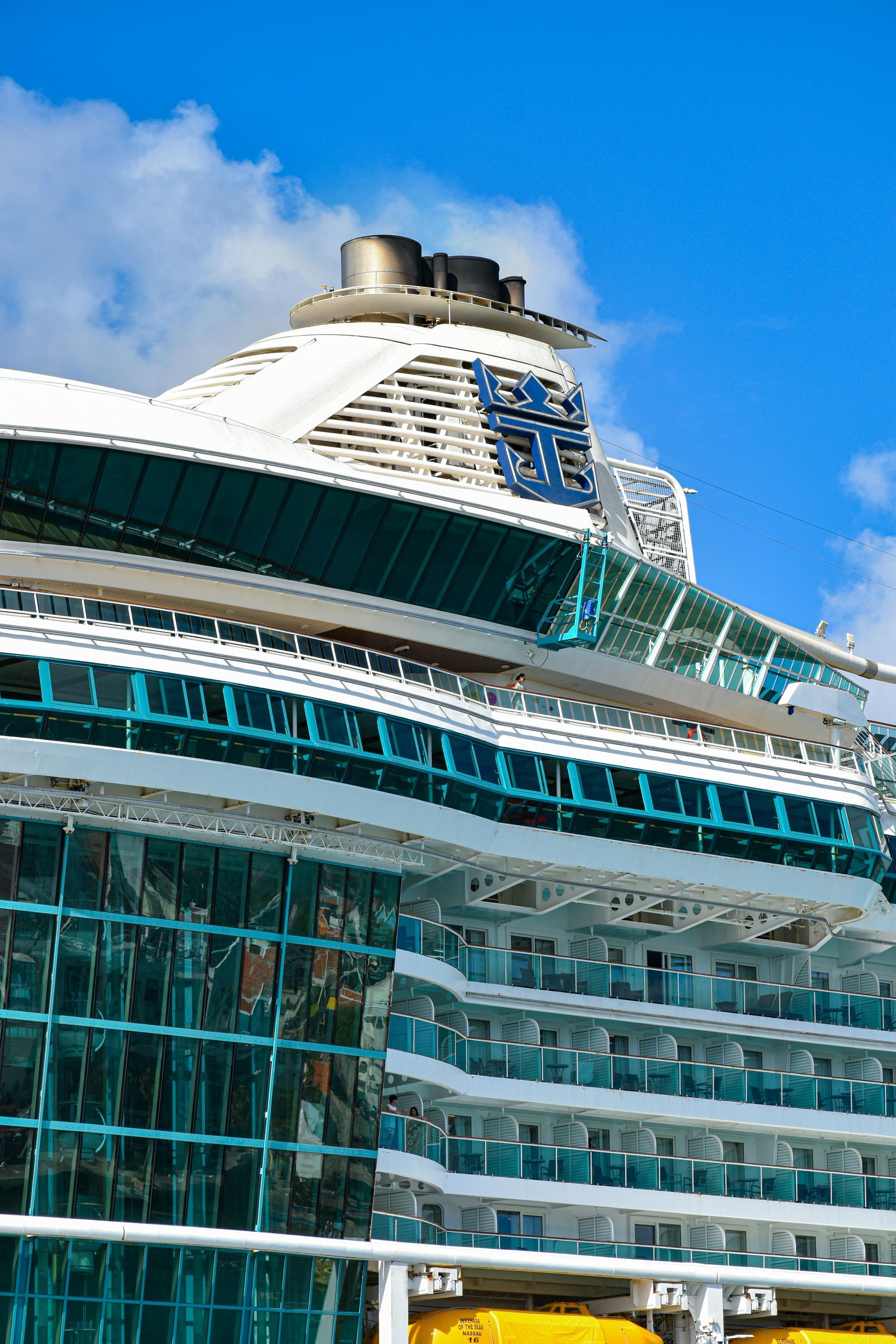 Cruise ship exterior with teal glass, white decks, and blue logo on top.
